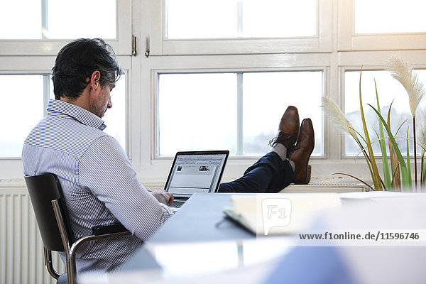 Mann mit Laptop am Fenster im Büro