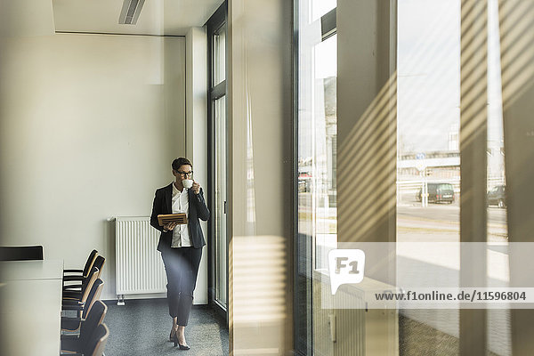 Businesswoman walking in office with coffee and tablet