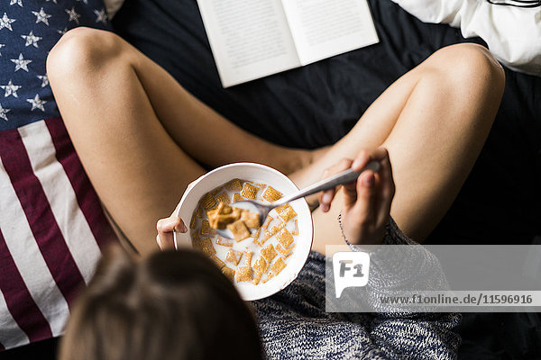 Draufsicht der jungen Frau  die Getreide isst und Buch liest