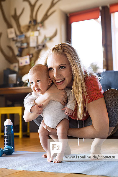 Lächelnde Mutter mit Baby und Fitnessgeräten zu Hause