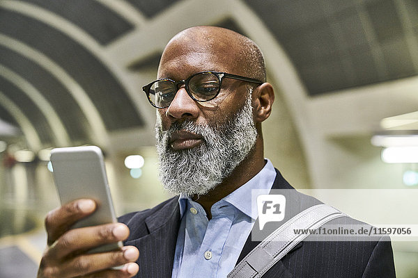 Geschäftsmann mit Smartphone-Lesemeldungen auf der Rolltreppe