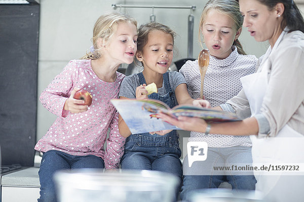 Mother and three girls in kitchen looking in book