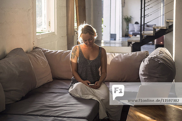 Blond woman sitting on the couch at looking at cell phone