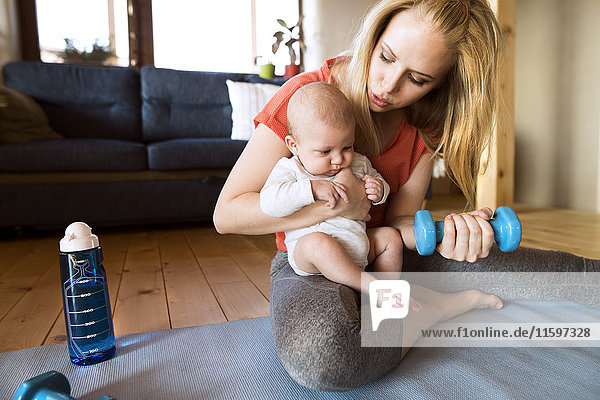 Mother with baby exercising with dumbbell at home