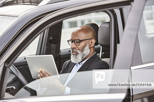 Businessman sitting in car using digital tablet