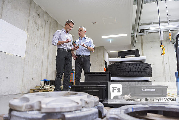 Two businessmen in factory hall with tyres examining product