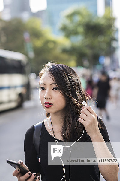 Porträt einer jungen Frau mit Kopfhörer und Handy  die etwas sieht.