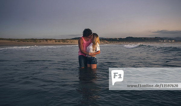Junges Paar  das sich in der Abenddämmerung im Meer küsst.