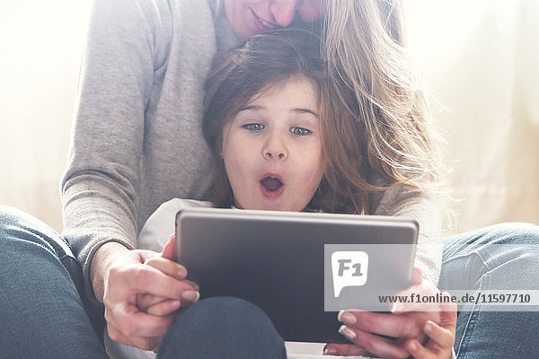 Portrait of astonished little girl using tablet with her mother