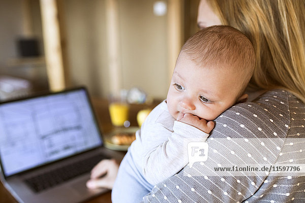 Mother with baby at home using laptop