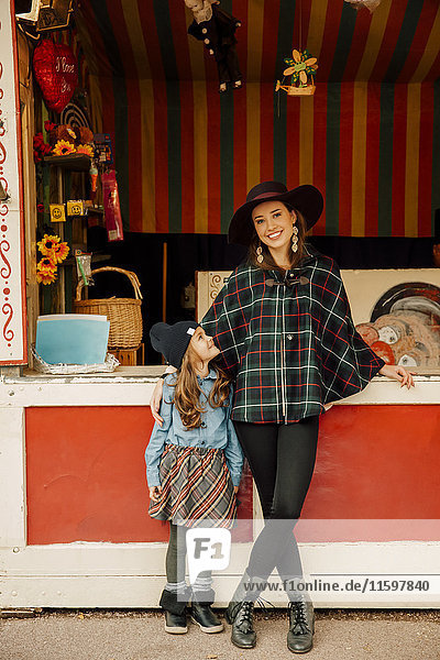 Young woman and little girl standing in front of stand at fair