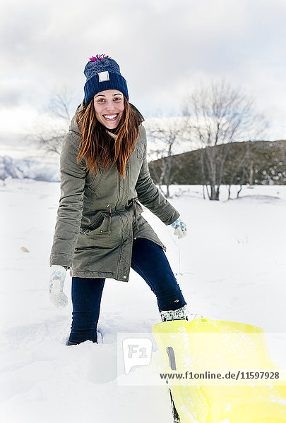 Porträt einer jungen Frau beim Schlittenfahren im Schnee