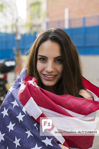 Porträt einer lächelnden jungen Frau in US-amerikanische Flagge gehüllt