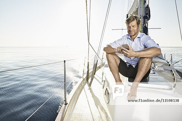 Smiling mature man sitting on his sailing boat using cell phone