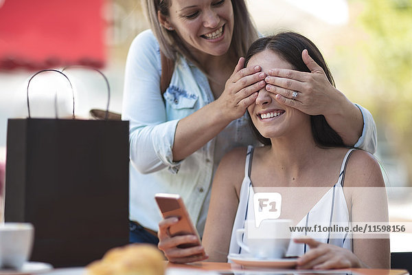 Woman covering eyes of her friend at an outdoor cafe