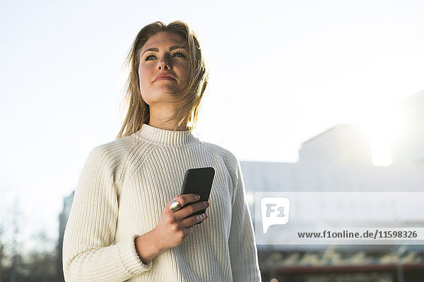 Portrait of young woman with cell phone looking at distance