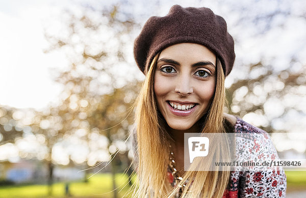 Porträt einer lächelnden jungen Frau mit Baskenmütze im Herbst