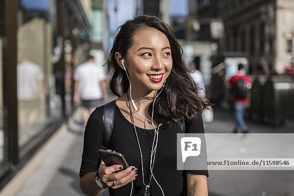 USA  New York City  Manhattan  junge Frau beim Musikhören mit Handy und Kopfhörer auf der Straße