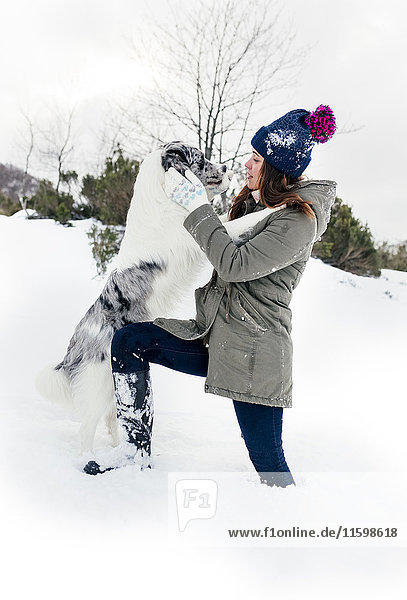 Junge Frau spielt mit ihrem Border Collie im Schnee