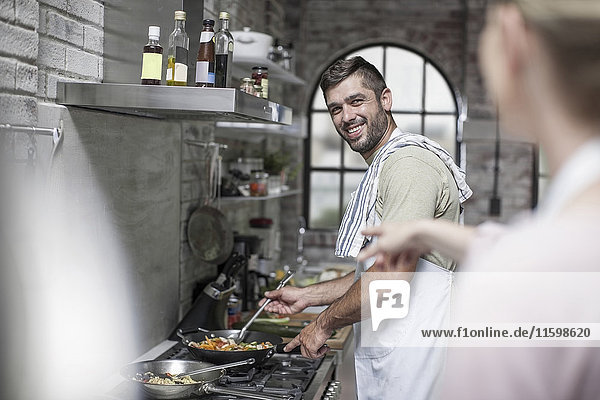 Lächelnder Mann beim Zubereiten des Essens mit Blick auf die Frau