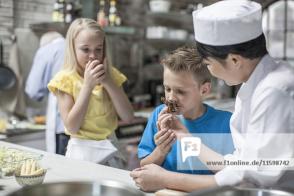 Junge und Mädchen riechen Essen von Köchin im Kochkurs
