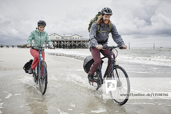 Germany  Schleswig-Holstein  St Peter-Ording  happy couple riding bicycle on the beach