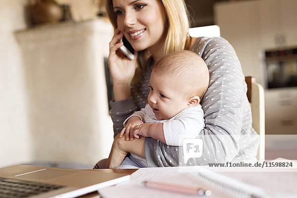 Lächelnde Mutter mit Baby zu Hause am Telefon