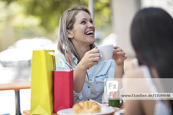 Zwei glückliche Frauen mit Einkaufstaschen in einem Outdoor-Café