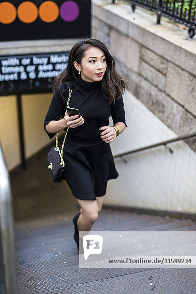 USA  New York City  Manhattan  junge Frau in schwarz gekleidet  die die Treppe hinaufgeht.