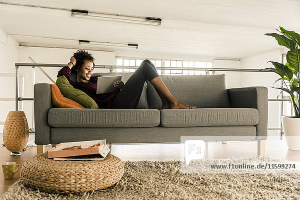 Lächelnde junge Frau auf der Couch liegend mit Tablette