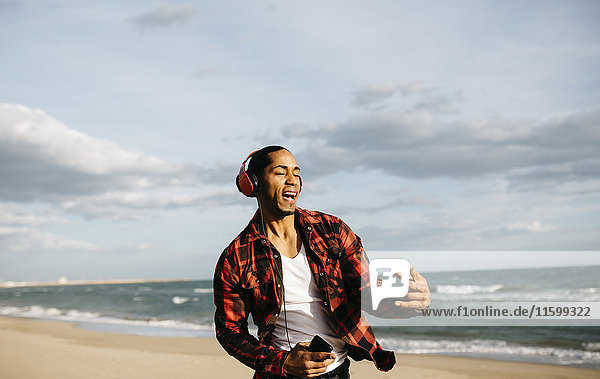 Porträt eines jungen Mannes am Strand  der beim Musikhören mit Kopfhörern singt und tanzt.