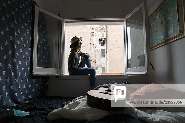 Junge Frau mit Hut im Fensterrahmen sitzend