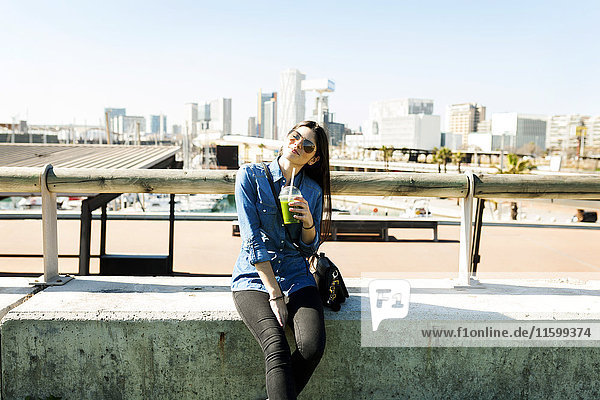 Spanien,  Barcelona,  lächelnde junge Frau mit Getränk im Sonnenlicht