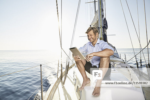 Lächelnder reifer Mann auf seinem Segelboot sitzend mit Tablette