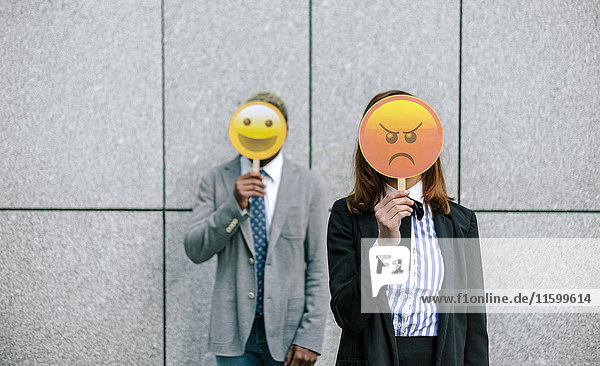 Junger Geschäftsmann und Frau  die Gesichter mit Emoji-Masken bedecken.