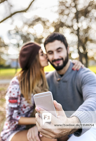 Couple taking selfie with smartphone in autumnal park  close-up