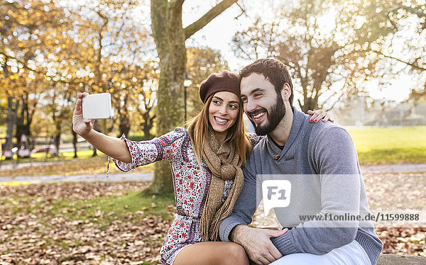 Happy couple taking selfie with smartphone in autumnal park