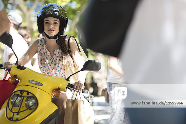 Junge Frau mit Einkaufstaschen auf Motorroller