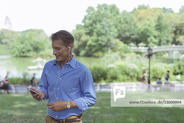 Man using cell phone and earphones in a park