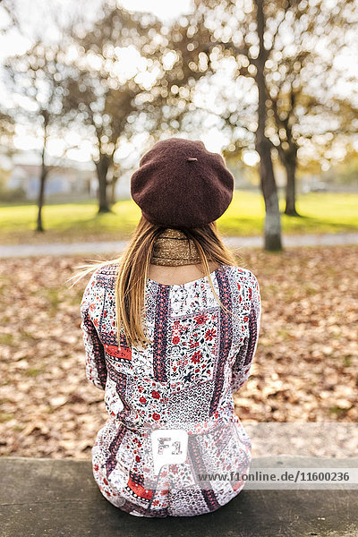 Back view of young woman wearing beret sitting on bench in autumn