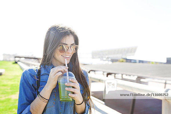 Spanien  Barcelona  Portrait einer lächelnden jungen Frau mit grünem Getränk