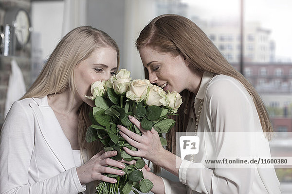 Zwei junge Frauen  die zu Hause Rosen riechen.