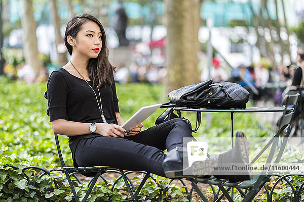 USA  New York  young woman with tablet sitting at city park