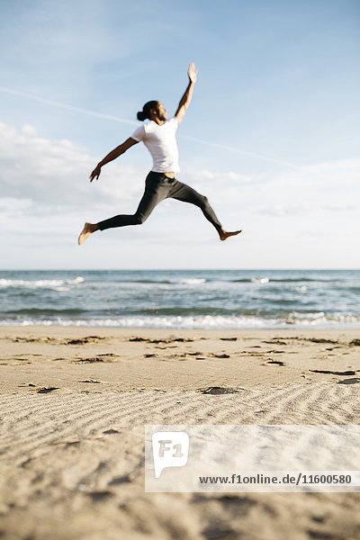 Junger Mann  der am Strand in die Luft springt.