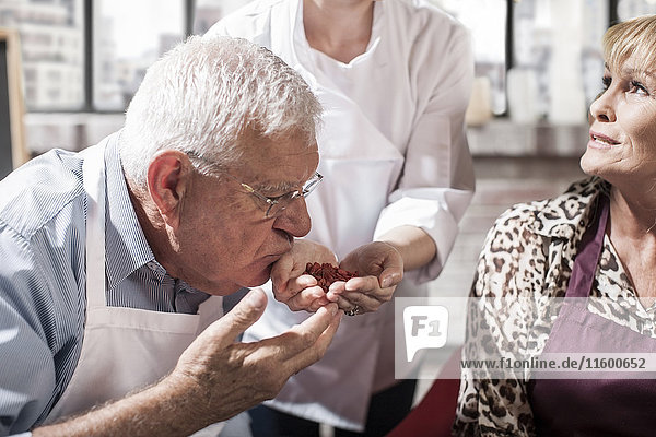 Senior Mann riecht Samen aus der Hand des Küchenchefs im Kochkurs