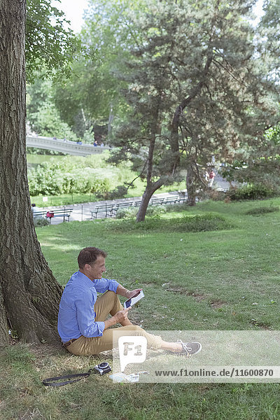 Mann mit Tablette auf einer Wiese im Park sitzend