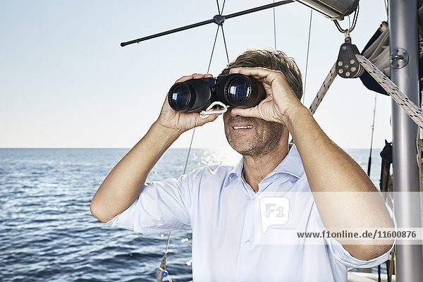 Mature man using binoculars on his sailing boat