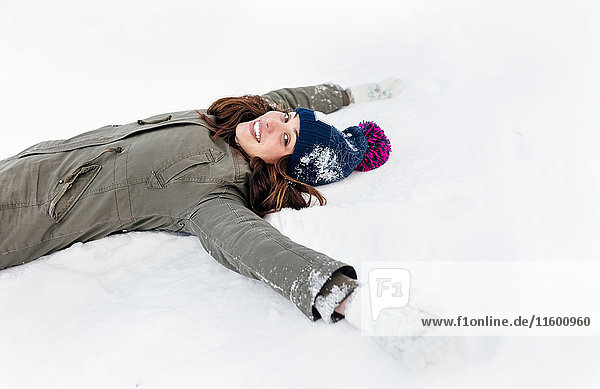 Lächelnde junge Frau im Schnee liegend