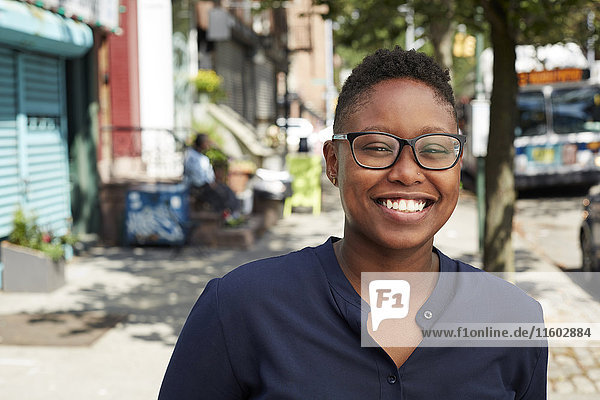 Schwarze Frau mit Brille lächelt auf dem Bürgersteig der Stadt