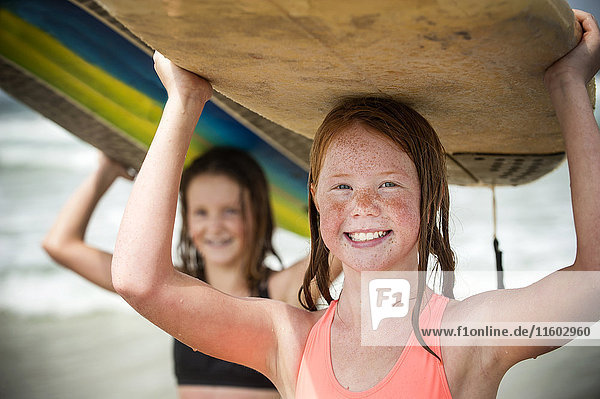 Portrait of smiling girls balancing surfboards on top of heads